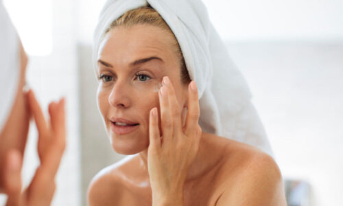 woman in towels looking in a mirror and putting face cream on