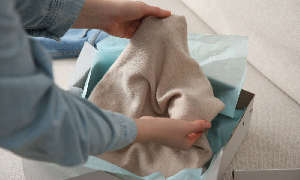 Woman taking soft cashmere sweater out of box indoors, closeup