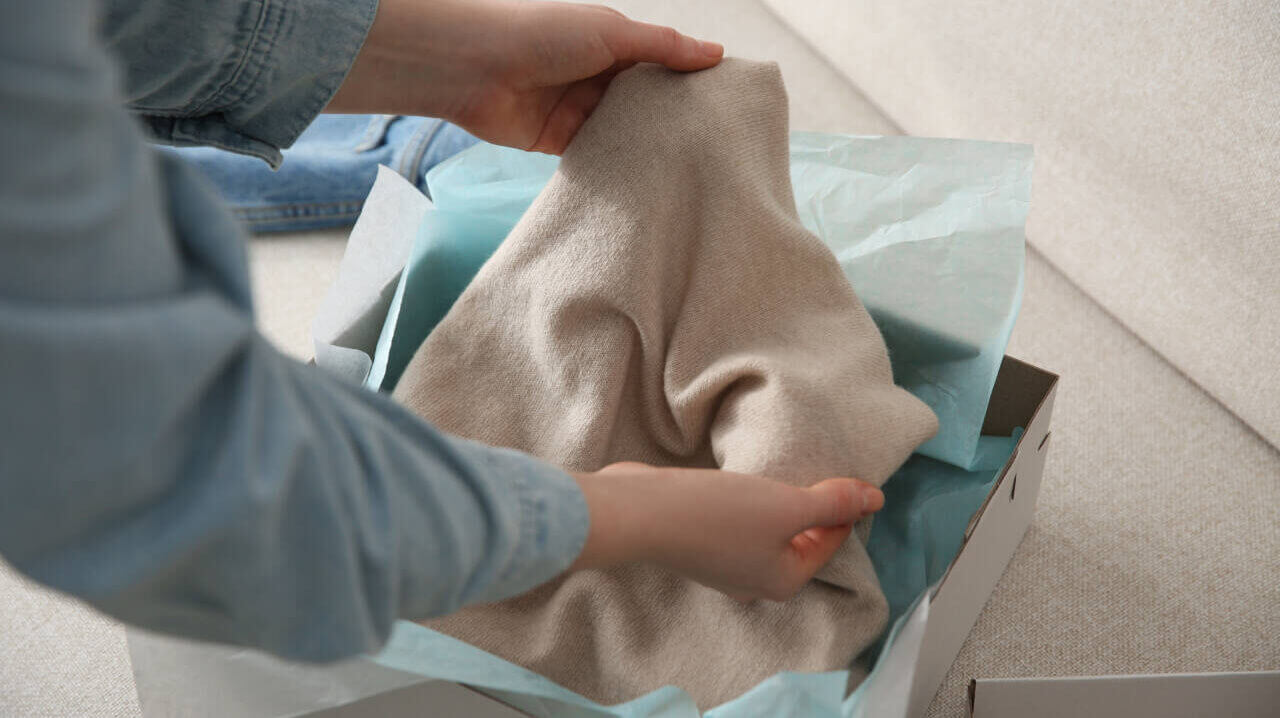 Woman taking soft cashmere sweater out of box indoors, closeup