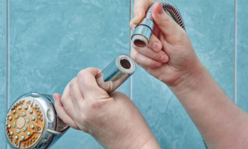 Female hands hold a broken shower head in the bathroom with blue tiles.